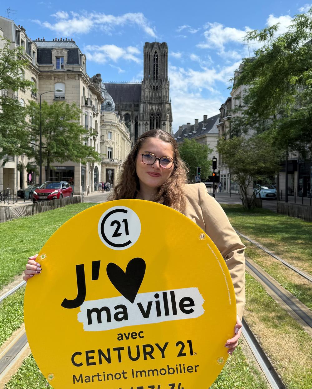 Maud Assistante de gestion en alternance chez Century 21 Martinot Immobilier avec sa veste or devant la cathédrale de REIMS