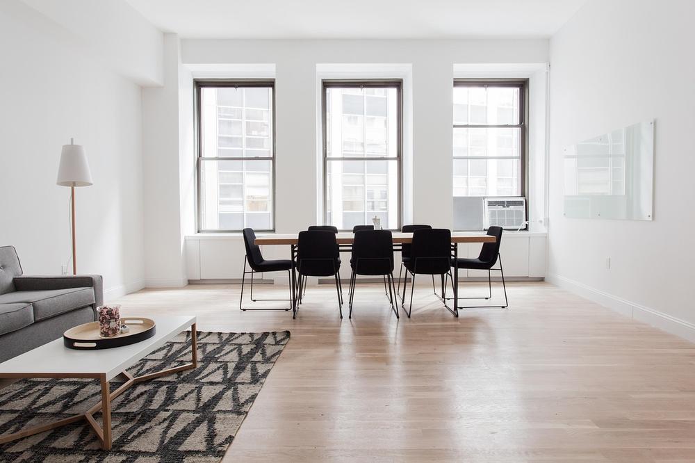 salon lumineux avec un canapé gris, une table basse blanche, un tapis, une table à dîner en bois et des chaises noires