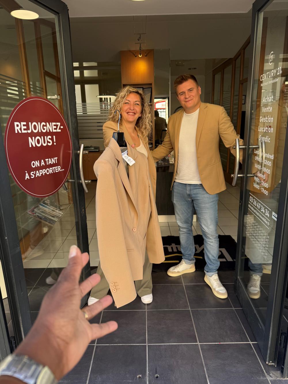 2 conseillers Century 21 Martinot Immobilier à REIMS, ouvrant les portes de l'agence au 9 rue des élus, pour tendre une veste or Century 21 à une nouvelle recrue 