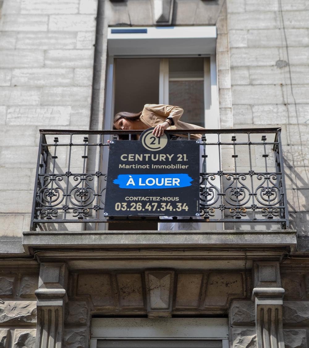 Inès, Conseillère location chez Century 21 Martinot Immobilier à REIMS, installation un panneau à louer sur un balcon